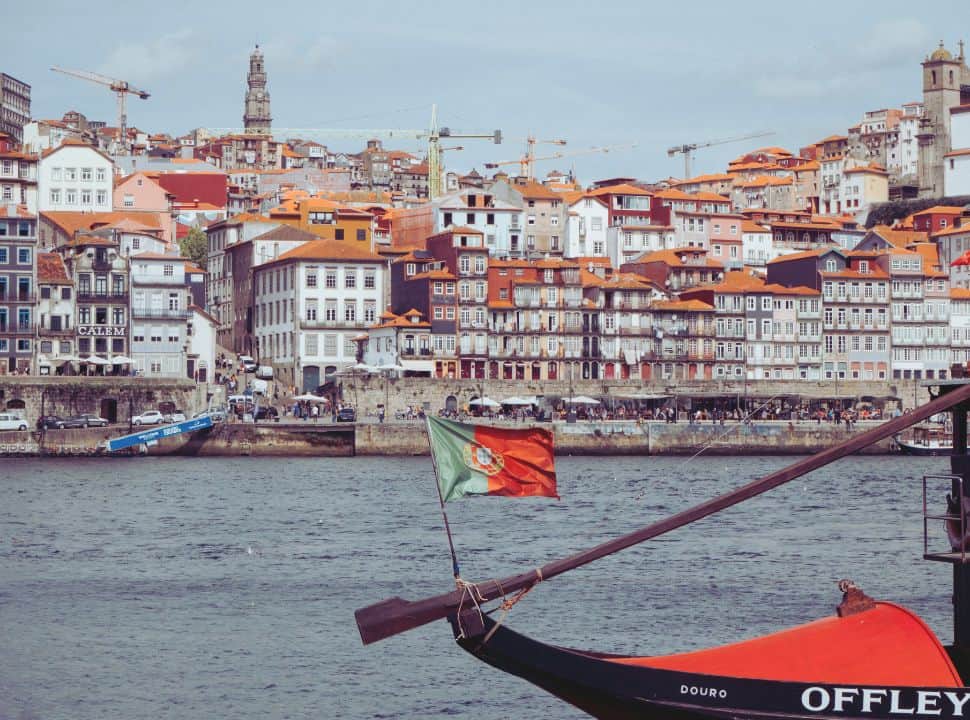 row of multiple story buildings along the river in Porto Portugal, on the hills clock towers are visible. 