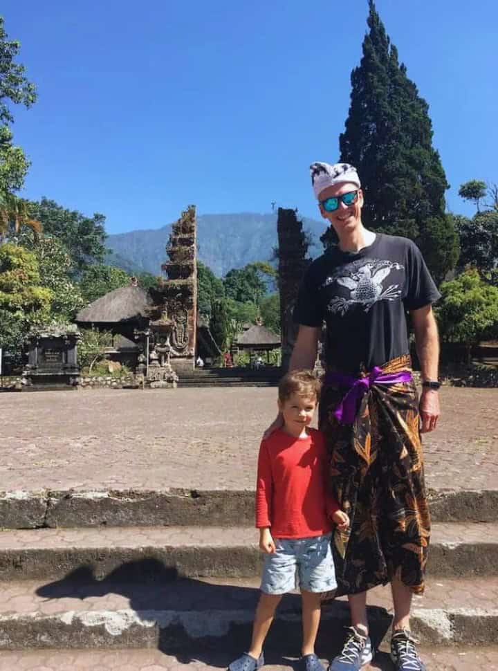 father and son standing in front of the entrance of Batukaru temple, the father is wearing a sarong and a headcloth which is mandatory when entering the temple