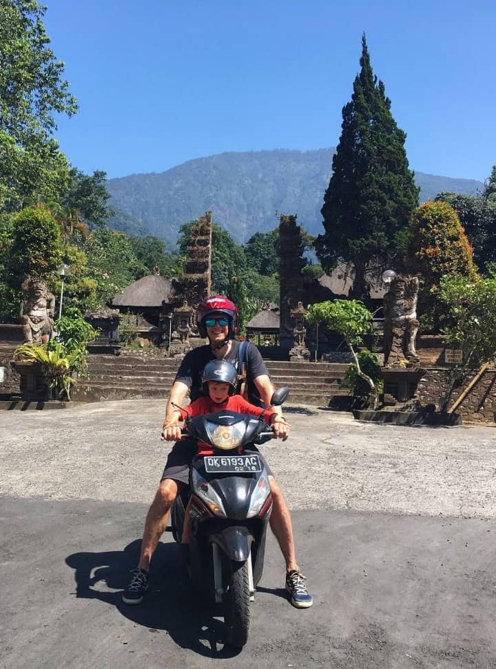 father and son on a motor scooter posing at the parking area of  Pura Luhur Batukaru with mount Batukaru in the back