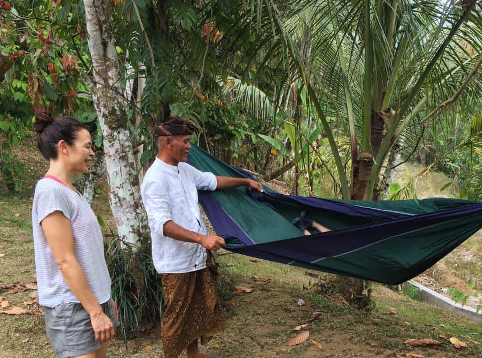 Pak Made, owner of Sari Devi Ecolodge in Bali holding the hammock with a boy in it, his mother is watching happily