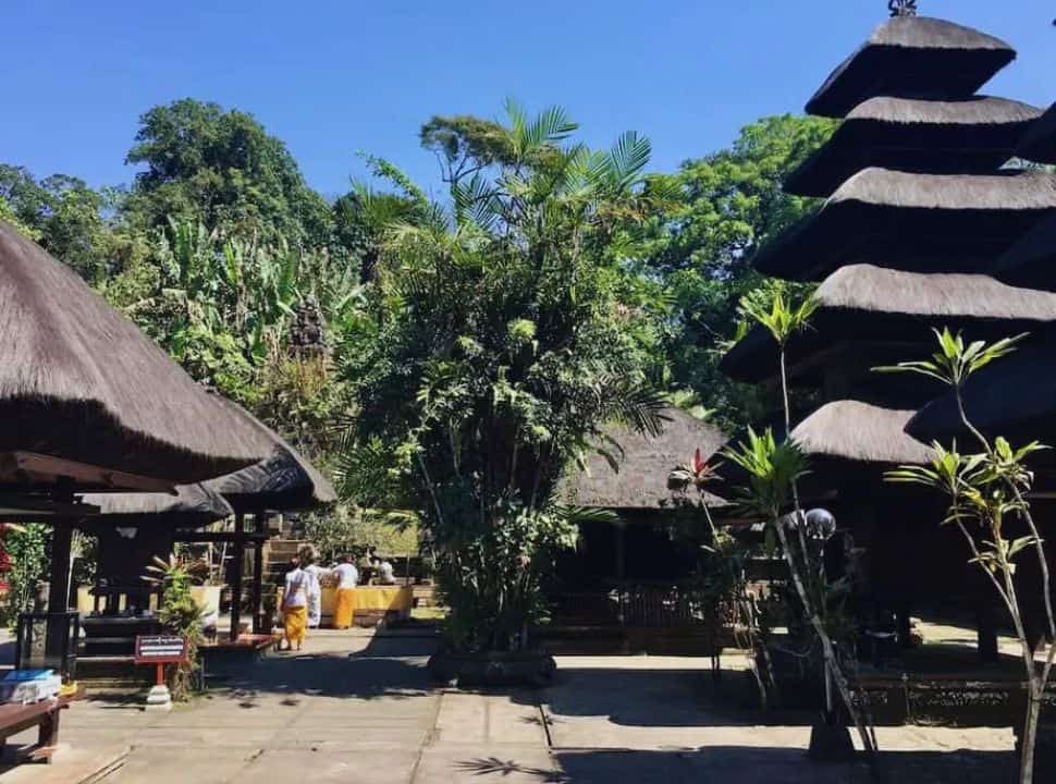 Balinese preparing for a ceremony in a distance at the temple courtyard where a multi tiered shrine is visible as several pavilions. 