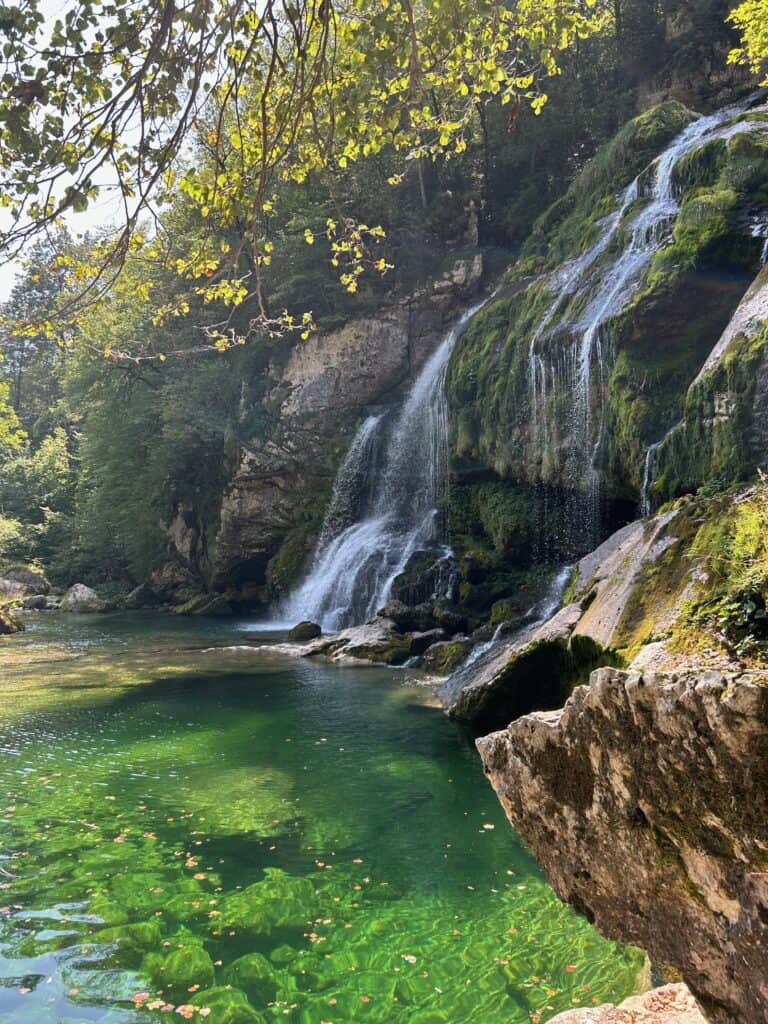 small waterfall with a clear green water pool surrounded by lush vegetation nearby bovec, a must stop on your slovenia 7 day itinerary