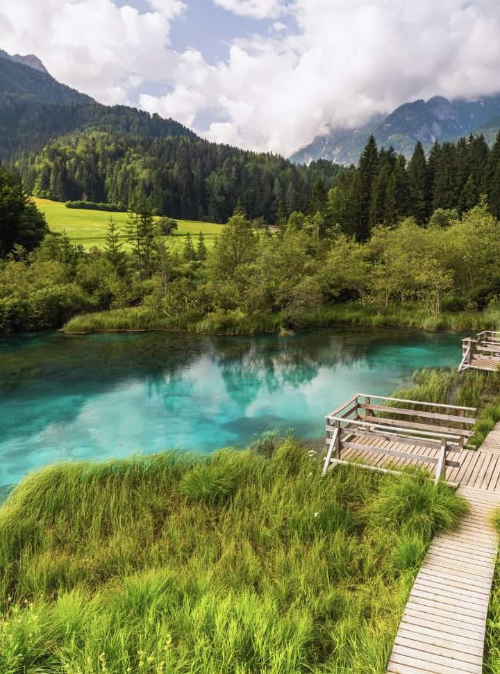 wooden walkway set along a emerald turqoise water surrounded by lush green forest in Slovenia