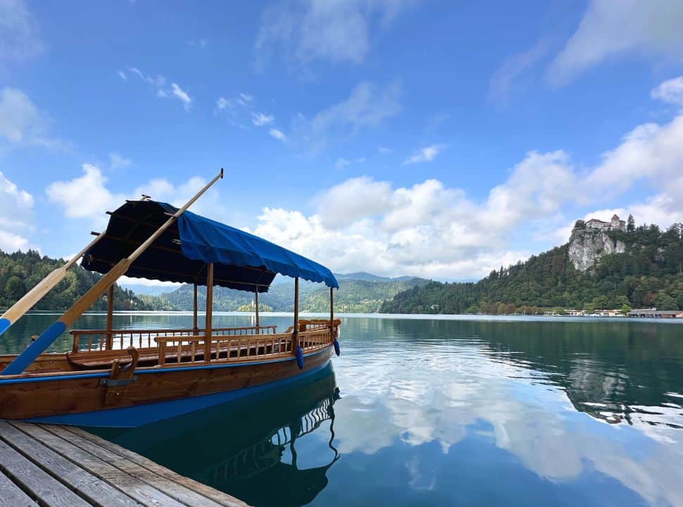 traditional wooden boat which can take a group of people docked at lake Bled with in the right Lake Bled and in the far distance the church on Bled island. 
