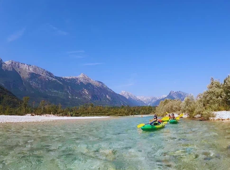 people kayaking down soca river near Bovec, with stunning mountain peaks in the background