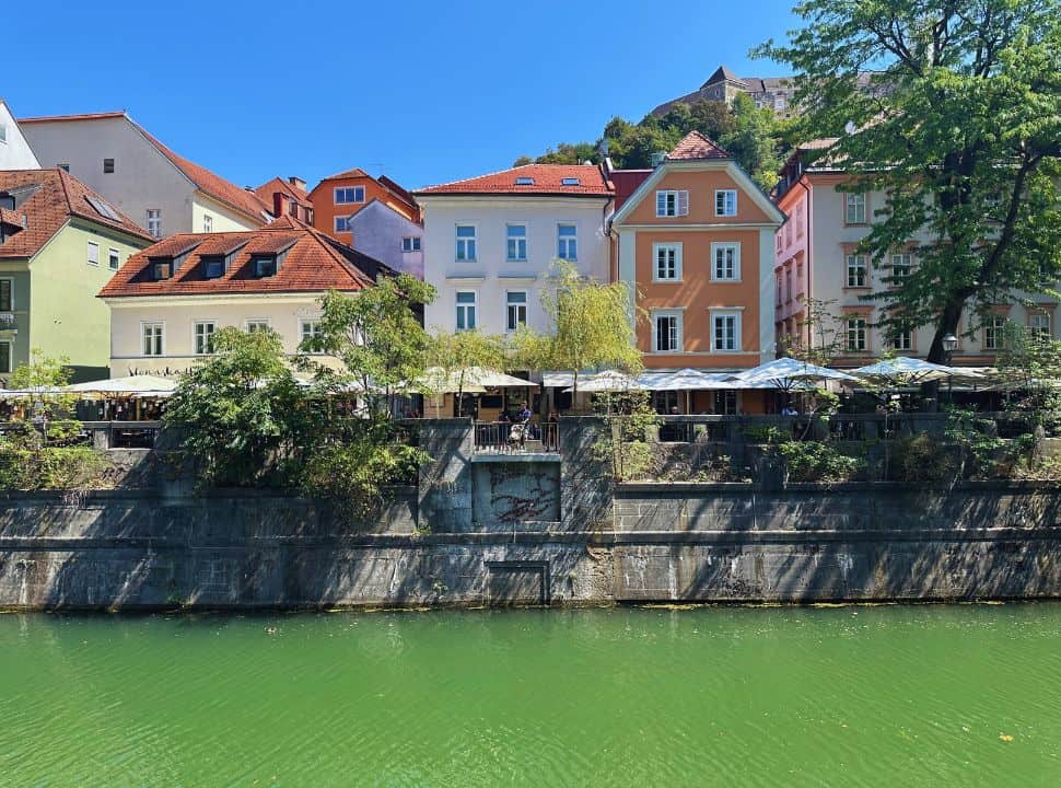 colorful buildings along the river in Ljubljana, in the far back the castle is visible on the mountain top