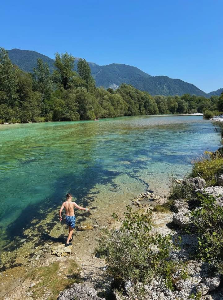 boy walking along the rocks of the river shore of the crystal clear Soca river in Slovenia