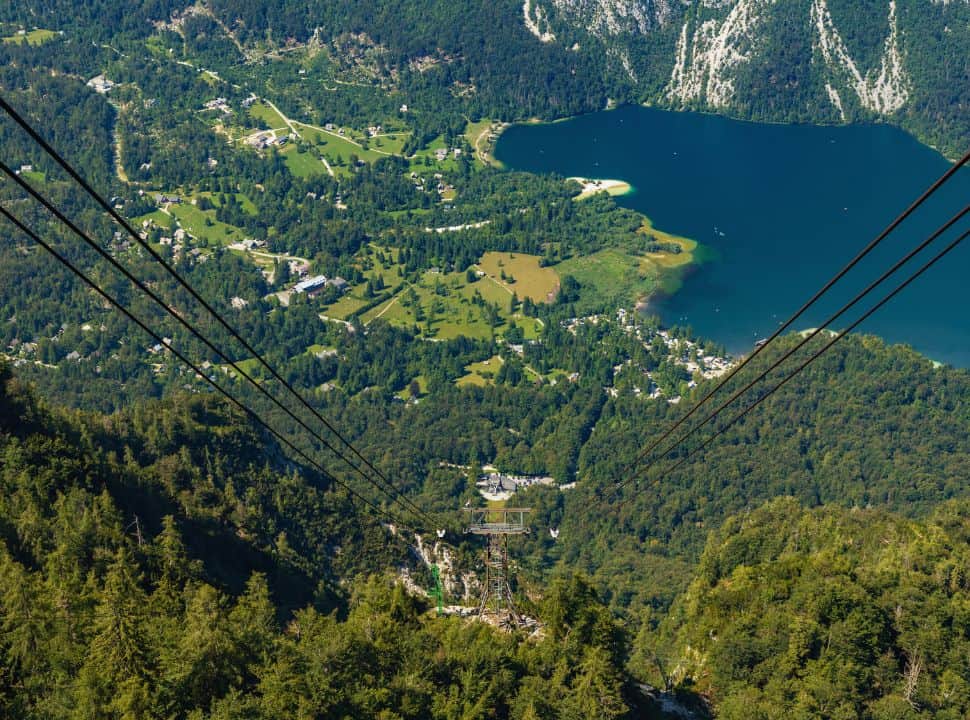 View of a cable car of Bohinj Lake which is  surrounded by mountains, green slopes and meadows.