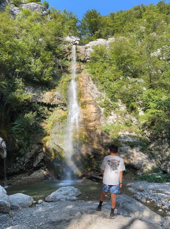 boy standing on the rocks looking at a natural waterfall and pool, a perfect things to do for you 7 day Slovenia itinerary