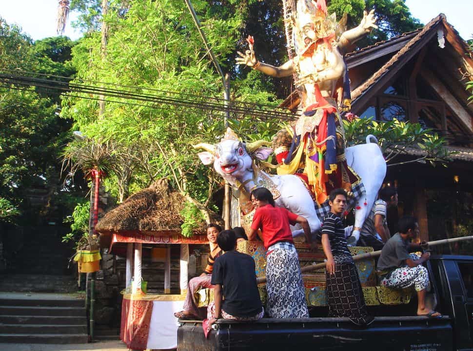 Balinese men on a truck stabilizing a statue off a god and a cow in the narrow street of Ubud Bali