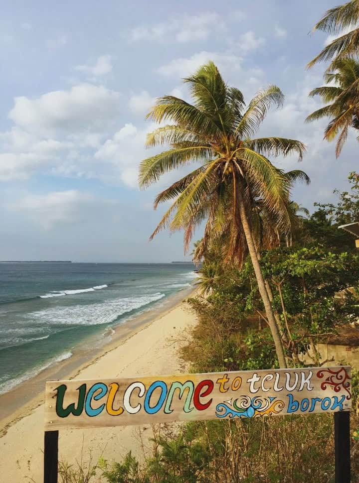 view of a beach with palmtrees in Lombok Indonesia, with the sign welcome to teluk borok painted in various colors