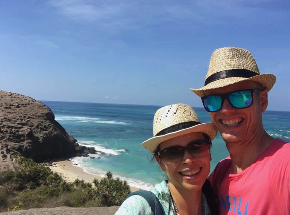 couple posing for a selfie near the coast line with in the back a small bay with a white sanded beach in Lombok Indonesia