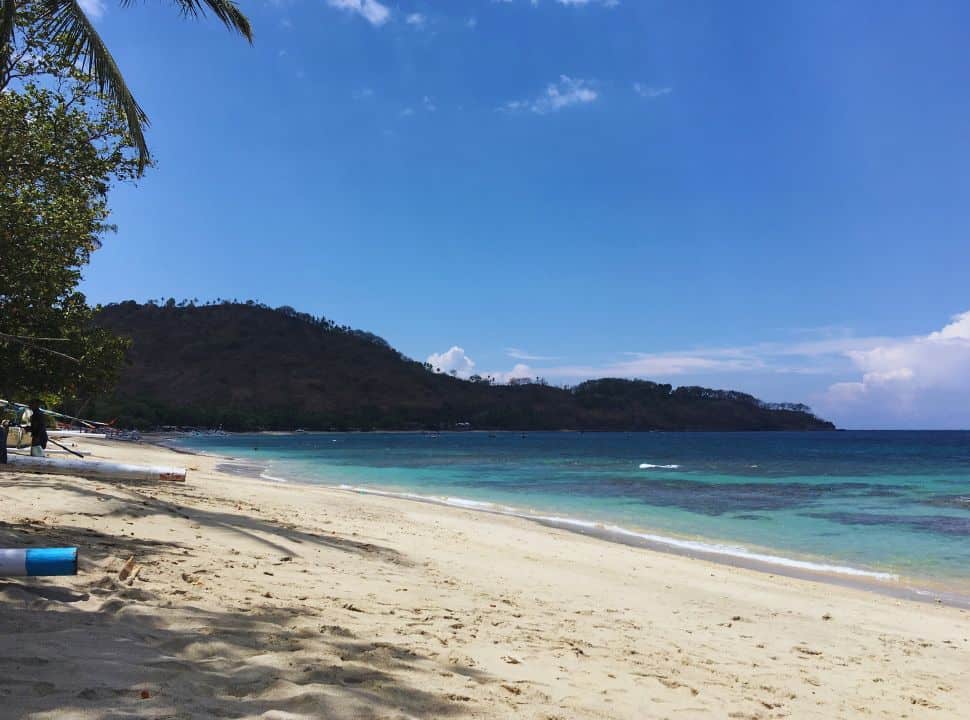 white sanded Lombok beach with turquoise blue water, fishing boats are at the beach other then that it is deserted