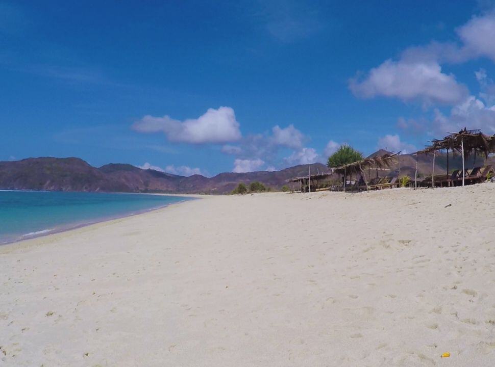 long stretched beach with soft sand, turquoise water and sun beds under a grass roof, all naturel
