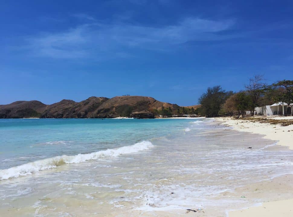 deserted white sanded beach with light blue water and hills in the back nearby kuta beach Lombok