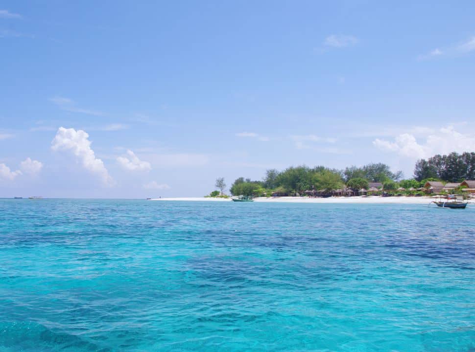 view from the clear blue ocean water of Gili Air, with its white strip of beach and several accommodation lined at the beach front