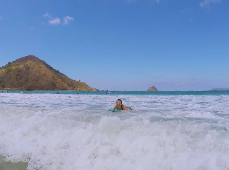 woman floating towards the beach on a body board while laughing out loud at Selong Belanak