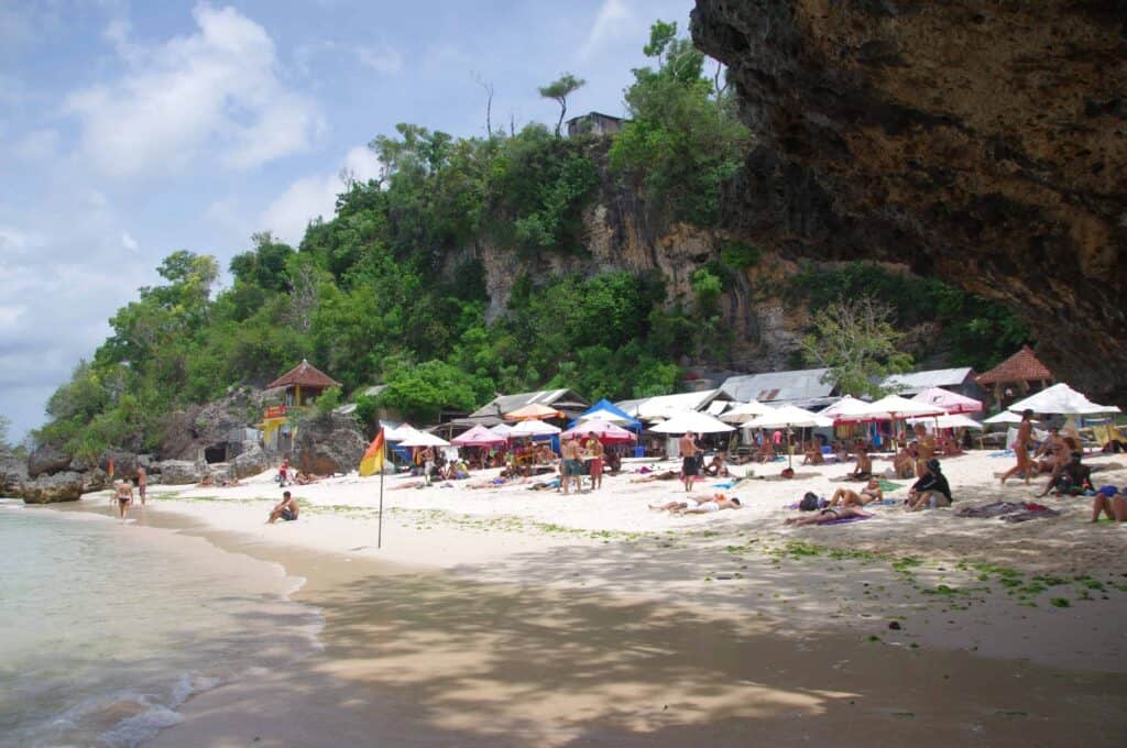 A small cove beach with white sand, sun umbrellas and beach goers enjoying the setting in the southern part of Bali