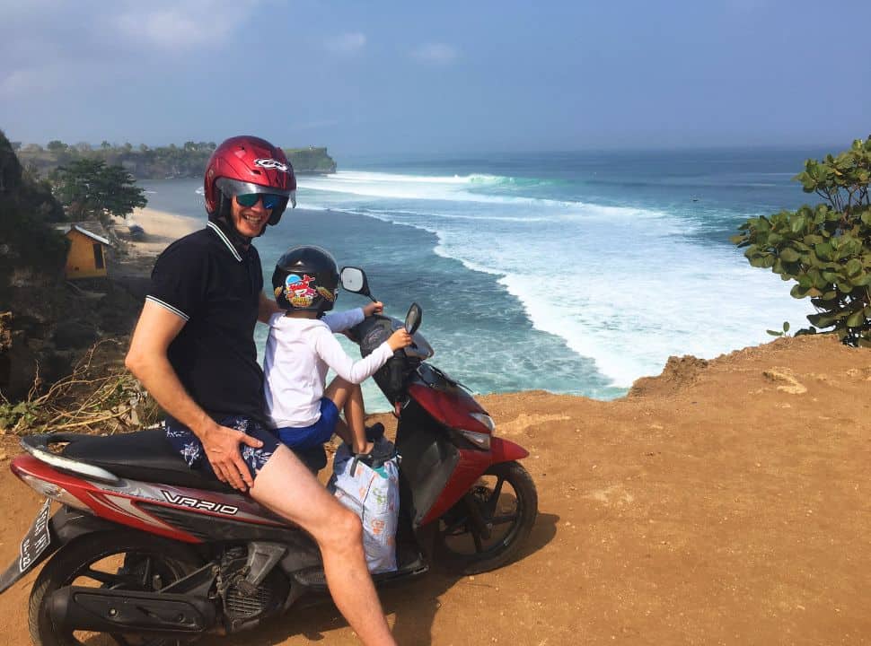 father and son on a motorbike standing on a cliff of Balangan beach Bali