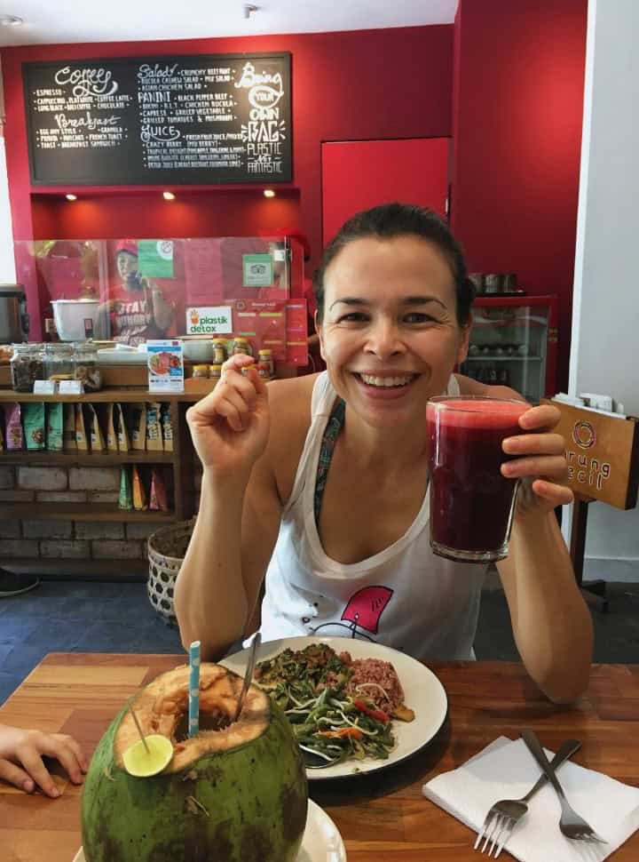 woman enjoying Indonesian food with a red colored vegetable juice and fresh coconut at one of the local restaurants in Sanur Bali