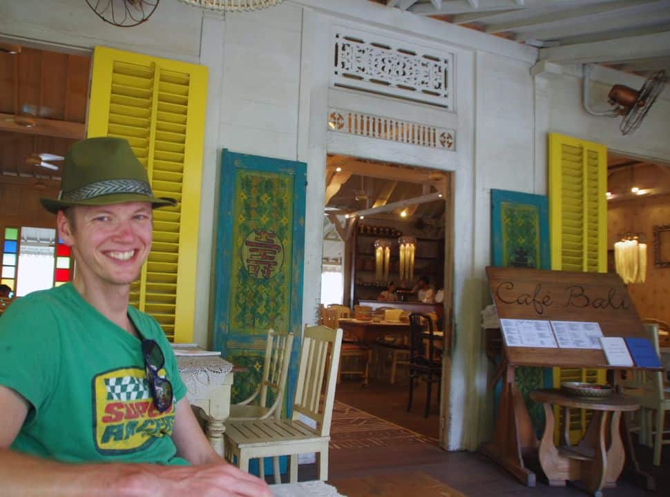 man sitting at a vintage looking restaurant with beautiful colored window shields and doors in Seminyak Bali