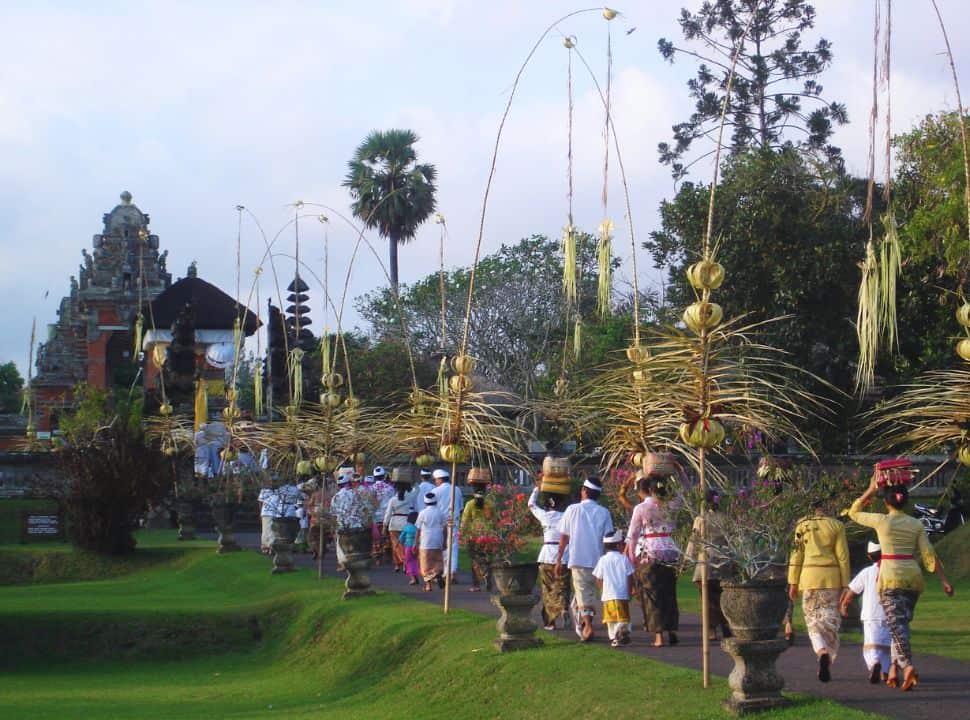 Balinese dressed in colorful traditional clothing carrying baskets and offerings on their heads making their way to the decorated temple in Mengwi Bali