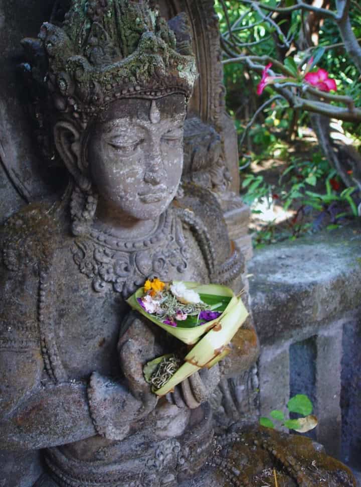 Balinese statue holding a colorful with flowers and banana leave offering in Bali