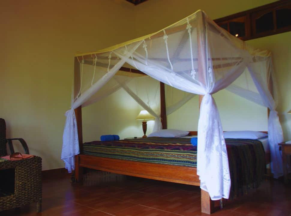 wooden double bed with traditional woven blanket and a mosquito net draped over the top of the bed in Bali