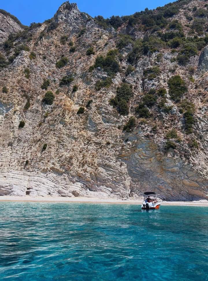boat approaching a narrow strip off beach with a cliffs towering over it at Corfu Greece