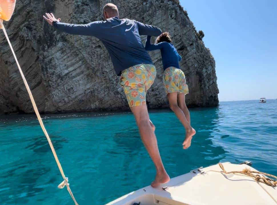 father and son in matching swimwear jump in to the clear blue ocean from the rental boat Corfu Greece