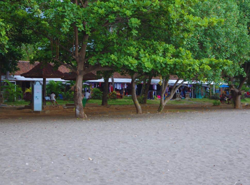 Lovina beach with a row of tree and shops in the far back