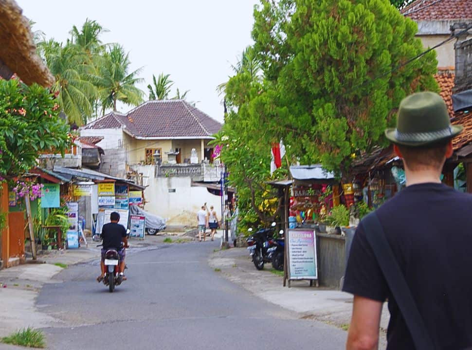 man walking along a quiet streets with shops and restaurants while a motorcycle is driving away in a distance in Lovina Bali
