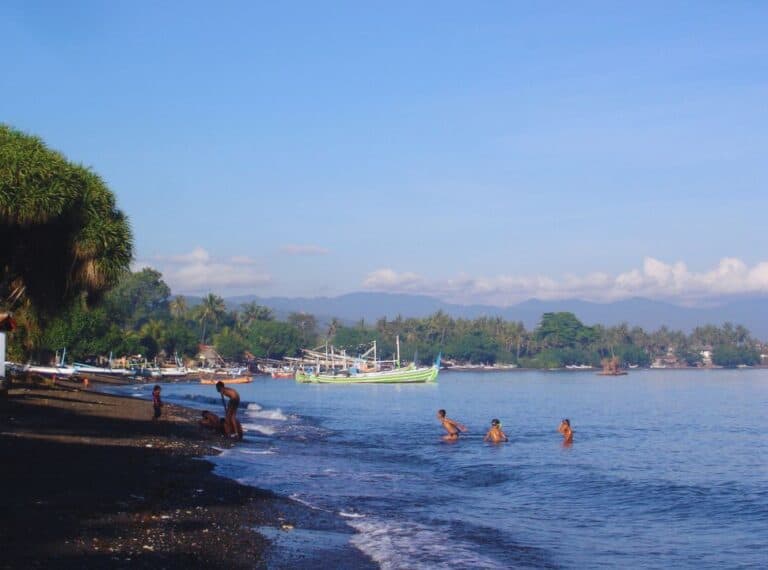 children swimming in the calm ocean water at lovina beach, where local fishing boats are set on the shore