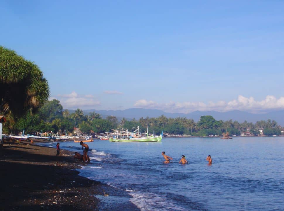 children swimming in the calm ocean water at lovina beach, where local fishing boats are set on the shore