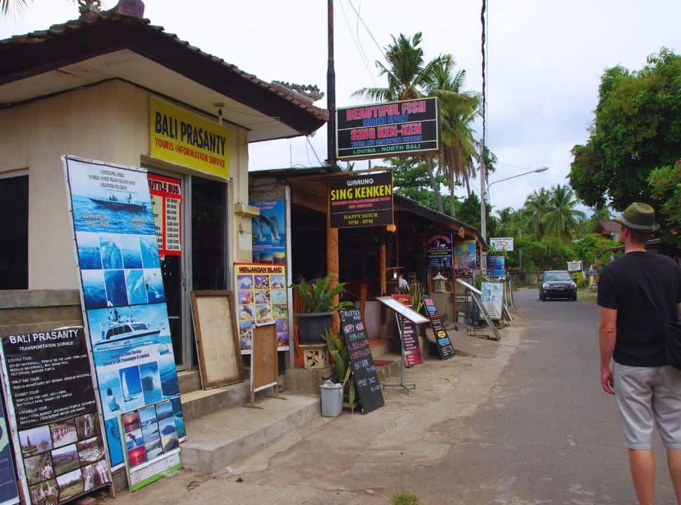 tourist looking at the many signs at a tourist agency offering all kinds of trips and transportation in Lovina Bali