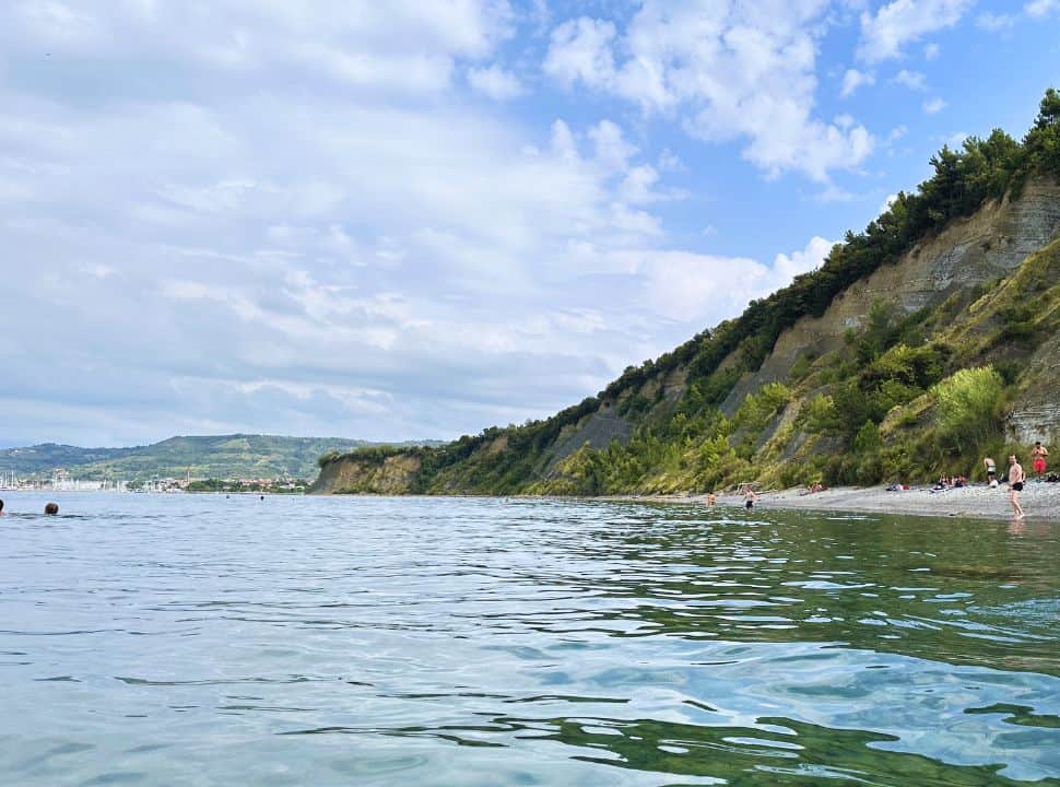 cliff beach with calm water, people swimming and sitting on the beach nearby Izola Slovenia