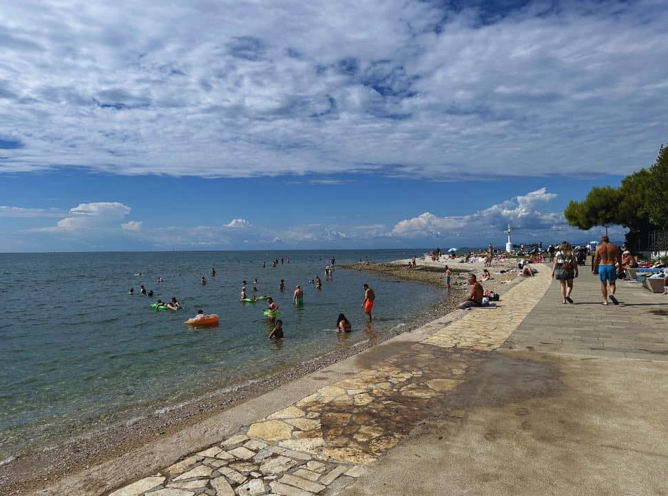 people enjoying the calm water and sitting along the promenade enjoying the sun in the small town Izola Slovenia