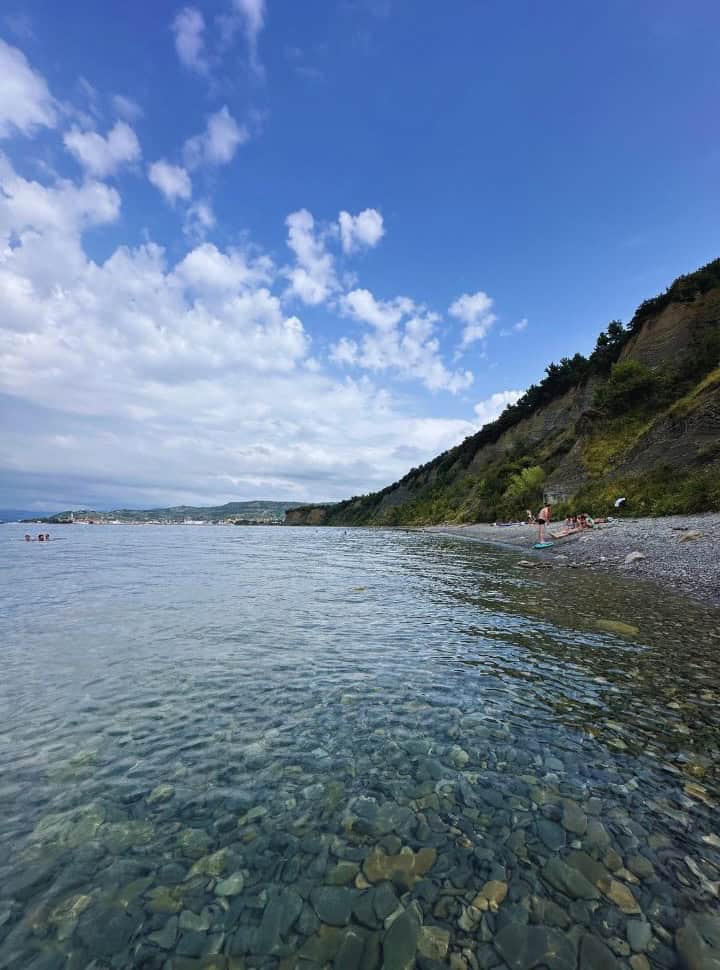pebbles visible in the clear ocean water along a bay with in far distance the small town Izola Slovenia