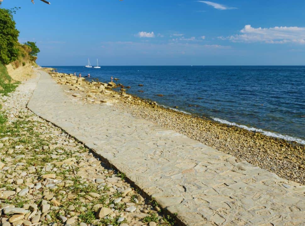 a quiet beach with large pebbles and a stone pavement nearby Piran Slovenia