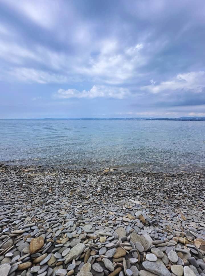 pebbles in all sizes at a crystal clear calm water in Slovenia, with in the far distance Italy.
