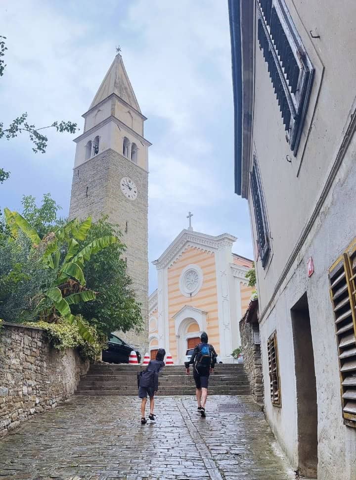 father and sun walking in the rain towards a church and church tower in Izola Slovenia