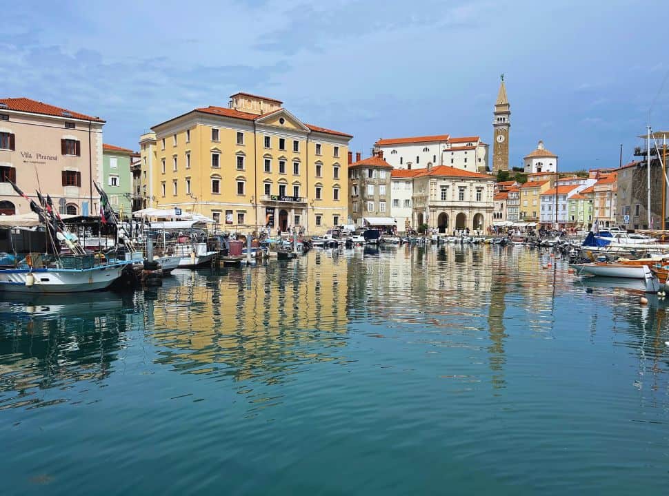 view of a small harbor set at a historic town with colorful buildings and a tall clock tower, Piran Slovenia