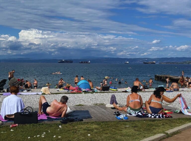 people sittingon the grass and ocean edge enjoying the sunny weather in Izola Slovenia