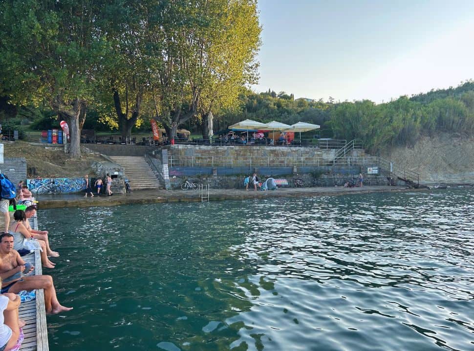 people enjoying the water by sitting on the docks and along the water at a beach nearby Izola Slovenia