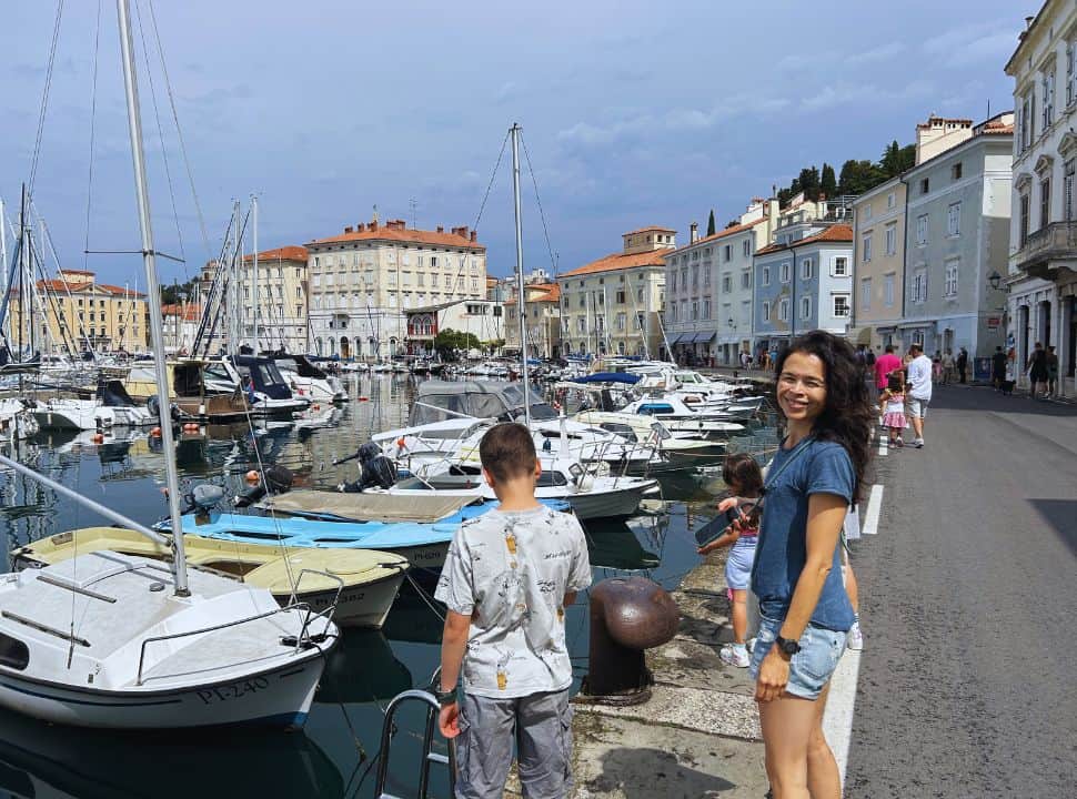 woman posing for picture at a harbor with small boats just outside Piran Slovenia where there are many old colorful buildings 