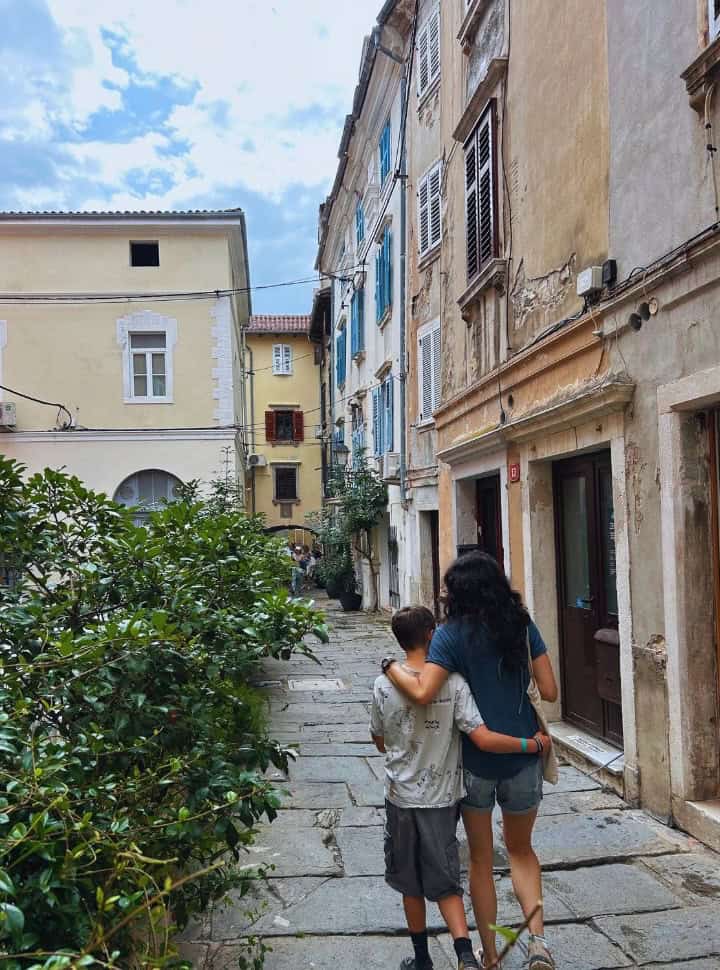 mother and son walking through a narrow streets with old colorful buildings in Piran Slovenia
