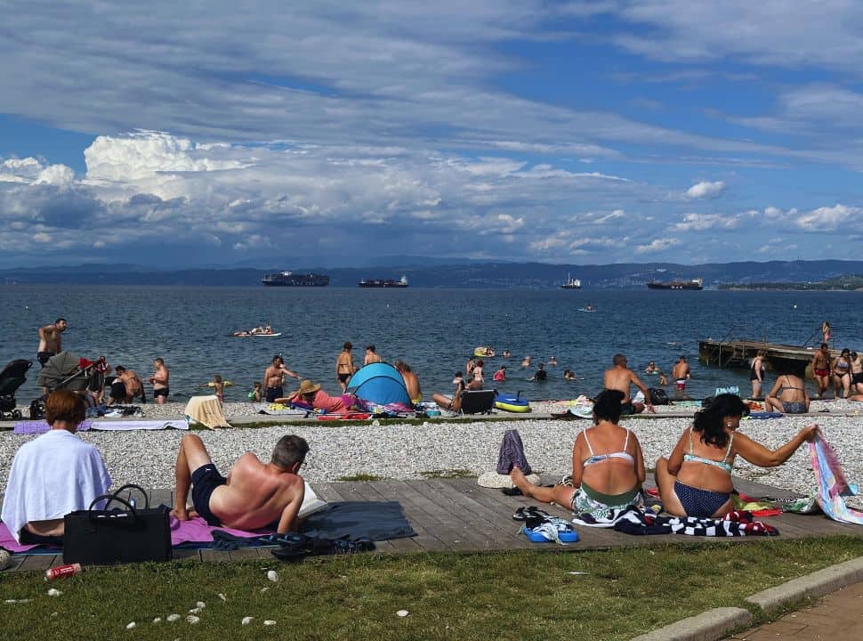 people sitting on the grass and wooden and pebbled beach in Izola Slovenia coast
